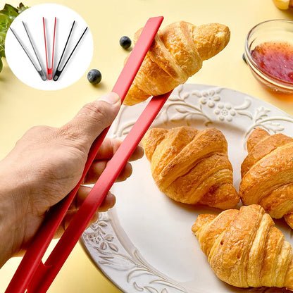 Person holding red tongs with croissants on a plate and additional croissants in the background.
