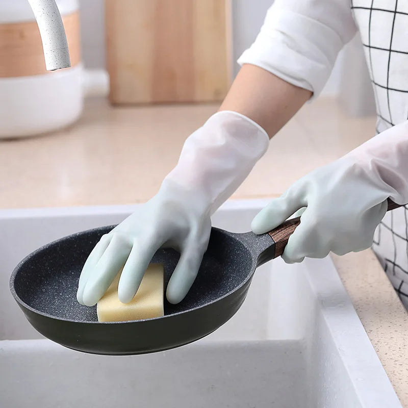 Person cleaning a frying pan with a bar of soap using gloves in a kitchen setting.