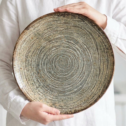 Person holding a large ceramic plate with concentric circle design in a kitchen setting