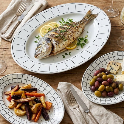 Dinner table setting with grilled fish, roasted vegetables, and olives.