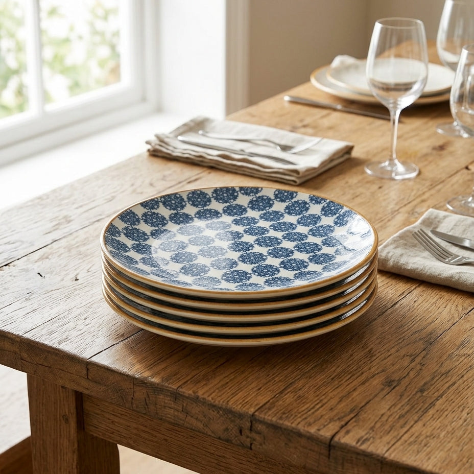 Stack of blue and white patterned plates on a wooden table with glasses and napkins.