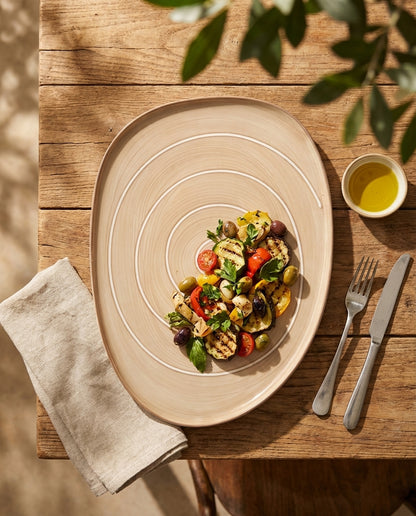 Plated dish of salad on a wooden table with a fork, knife, and small bowl of oil.