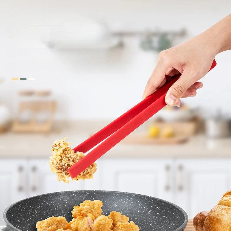 Person using red tongs to serve fried food from a pan in a kitchen setting