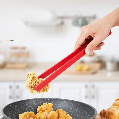 Person using red tongs to serve fried food from a pan in a kitchen setting