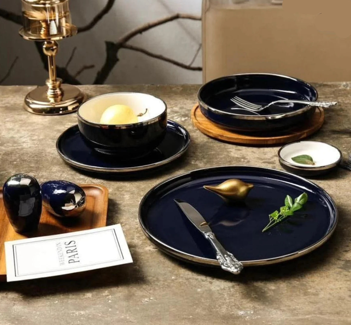 A set of dark blue porcelain dinnerware with silver rims displayed on a table, including plates, a bowl, and silverware.