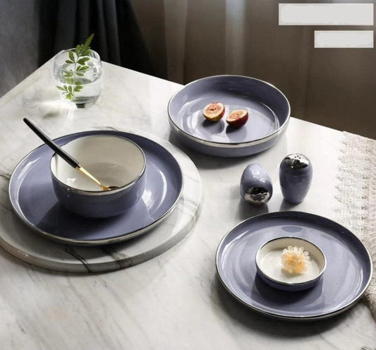 A set of gray porcelain dishes with silver rims displayed on a table, including plates, bowls, and dishes with food on them.