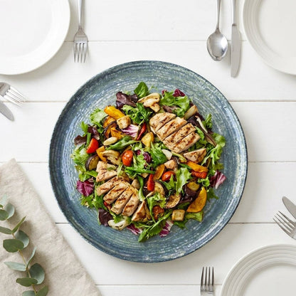 Salad with grilled chicken and vegetables on a blue plate, set on a white table.