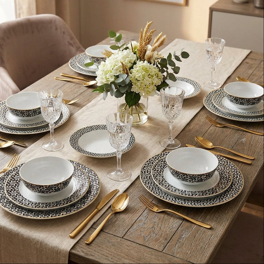 Dining table set with patterned plates, gold cutlery, and a vase of flowers in a home setting.