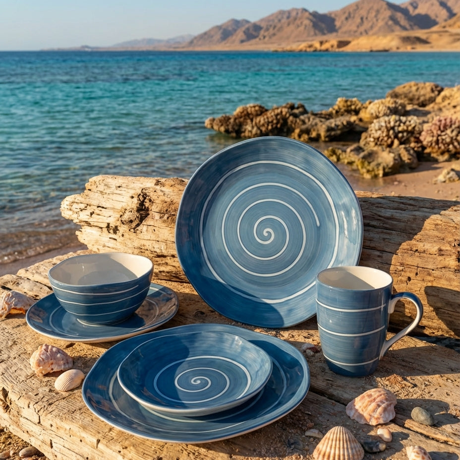 Blue ceramic tableware set on a wooden surface by the sea with mountains in the background