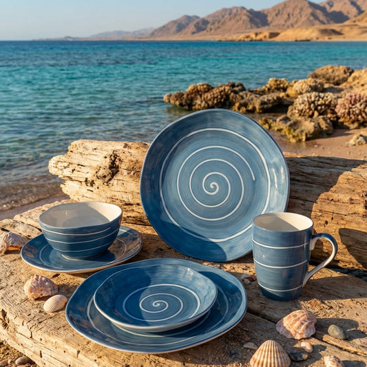 Blue ceramic tableware set on a wooden surface by the sea with mountains in the background