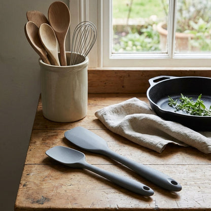 Kitchen utensils including wooden spoons and a whisk in a container on a wooden counter.