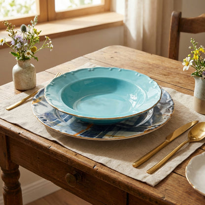 Set of blue ceramic plates on a wooden table with gold cutlery and floral arrangements.