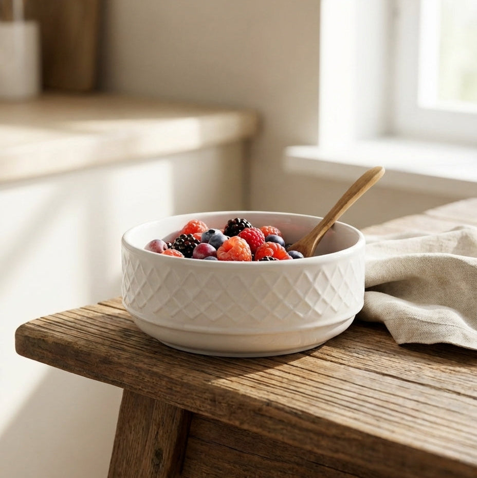 White bowl with fruits on a wooden table near a window