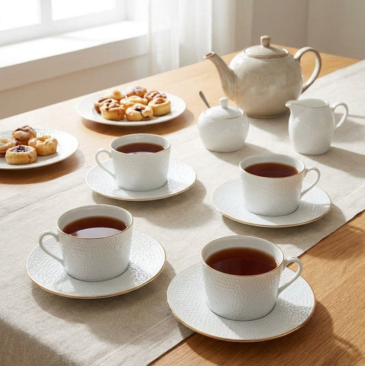 Tea set with cups, saucers, a teapot, and pastries on a wooden table.