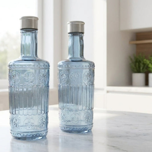 Two blue glass bottles with silver caps on a marble countertop in a kitchen.