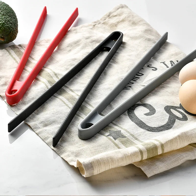 Three pairs of tongs in red, black, and gray on a kitchen towel.
