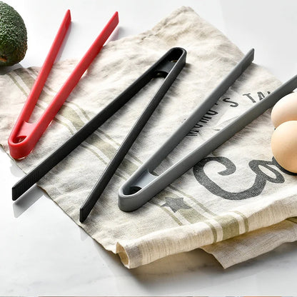 Three pairs of tongs in red, black, and gray on a kitchen towel.