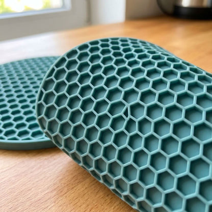 A close-up of a teal silicone roll-up mat with a raised honeycomb pattern, resting on a light wood tabletop with a second matching mat partially visible in the background.