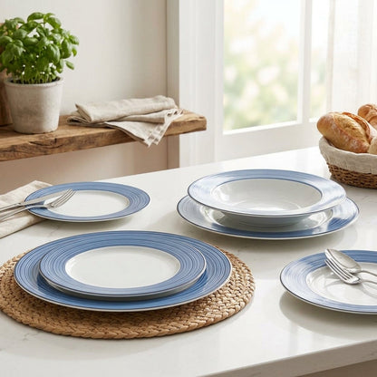Blue and white ceramic dinnerware set on a table with a plant and bread in the background.