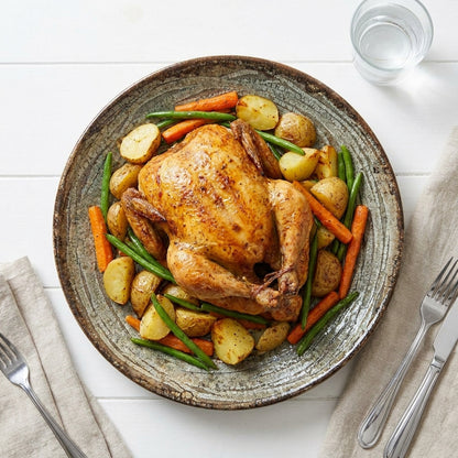 Roasted chicken with vegetables on a ceramic plate with cutlery and a glass of water.