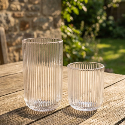 Two ribbed glass tumblers on a wooden surface with a natural outdoor background.