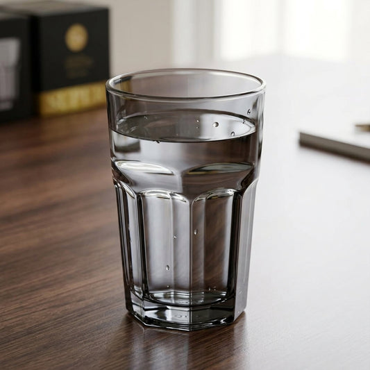 A clear glass tumbler with a fluted lower section, partially filled with water, sitting on a dark wooden tabletop.