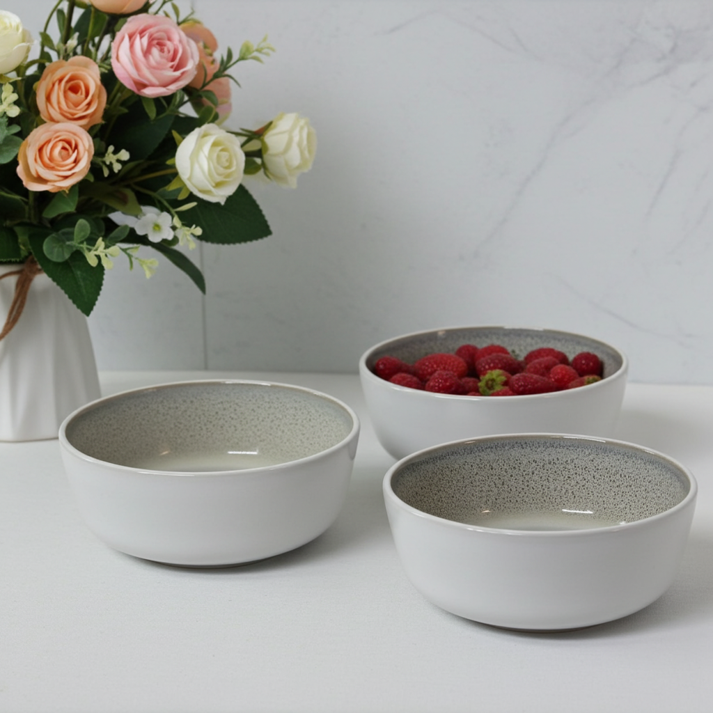 Three ceramic bowls with textured interior on a white surface, one containing raspberries, with a vase of flowers in the background.