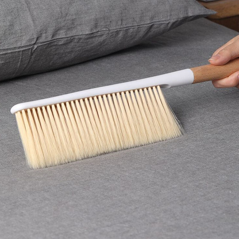 A hand holding the Eazi Cleaning Brush with a long wooden handle over a grey surface, demonstrating its use for cleaning.