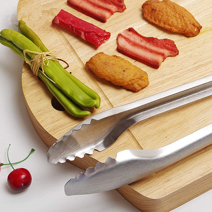 Wooden cutting board with food items and metal tongs on a white background