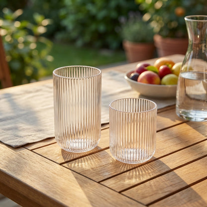 Two clear glass tumblers on a wooden table with a blurred garden background