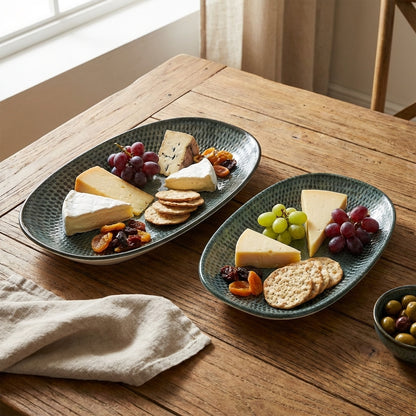Two green ceramic platters with cheese, crackers, and fruits on a wooden table.