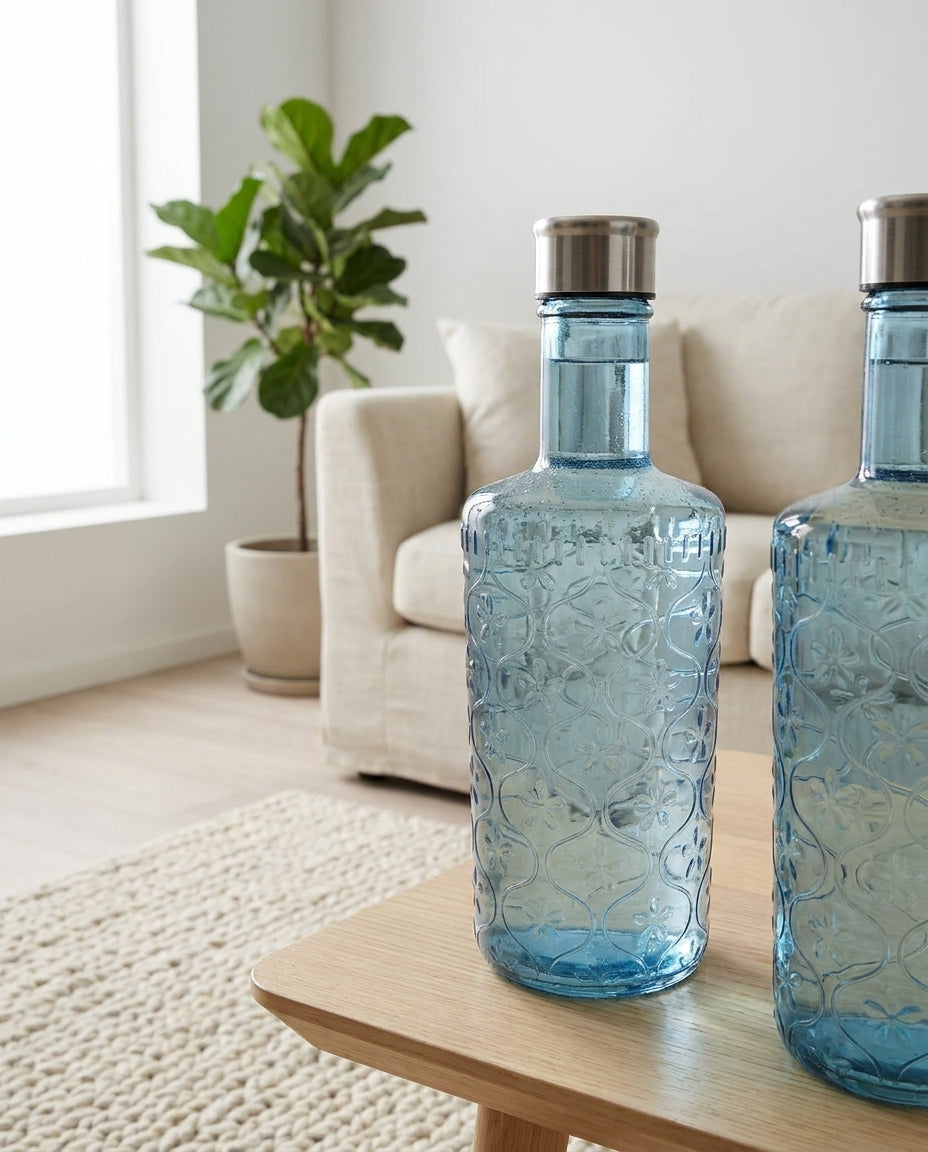 Two blue glass bottles with silver caps on a wooden table in a living room.