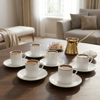 Café au lait served in white cups with saucers on a wooden table, with a gold coffee pot and snacks in the background.