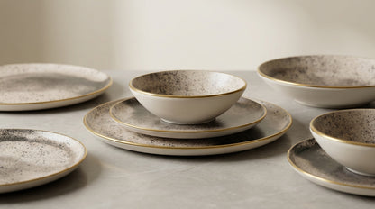 Set of ceramic dinnerware with speckled glaze on a neutral background