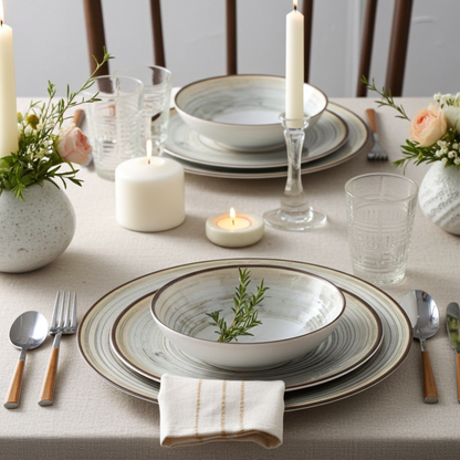 Elegant table setting with plates, candles, and flowers on a light gray tablecloth.