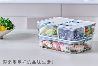A person holding a square-shaped food storage container with a blue silicone lid, in a refrigerator filled with various other containers.