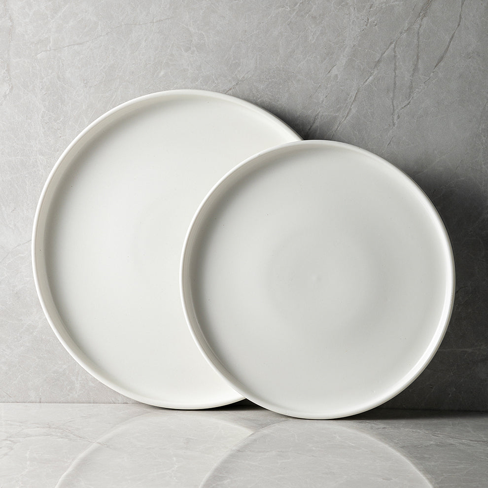 A set of white porcelain plates of two different sizes placed on a marble surface.
